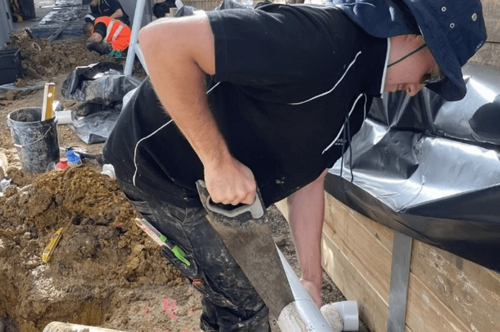 Plumber installing an outdoor drain on residential construction site