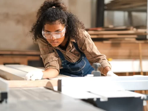 Portrait, female multiracial carpenter working in woodshop small business. Afro woman with goggles standing in DIY carpentry workshop with confidence. Empowerment joiner women in woodworking industry